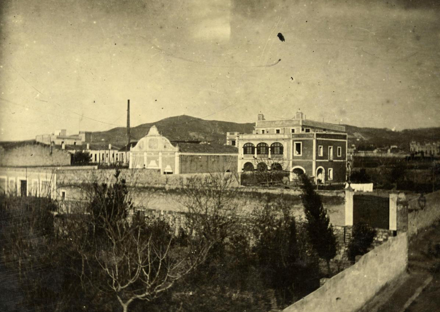 1897 AMDS Vista d_un recinte enmurallat amb arbres davant de can Nicasi, situat al carrer de Miquel Àngel. Al fons, la serra de Collserola.