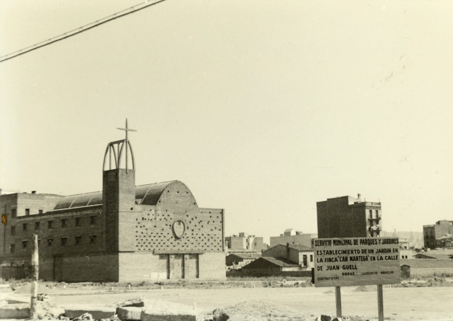 1961 AMDS En primer terme, un rètol situat al carrer de Joan Güell. Al fons, la parròquia de Sant Joan Maria Vianney. Autor Peris i Xancó, Jaume