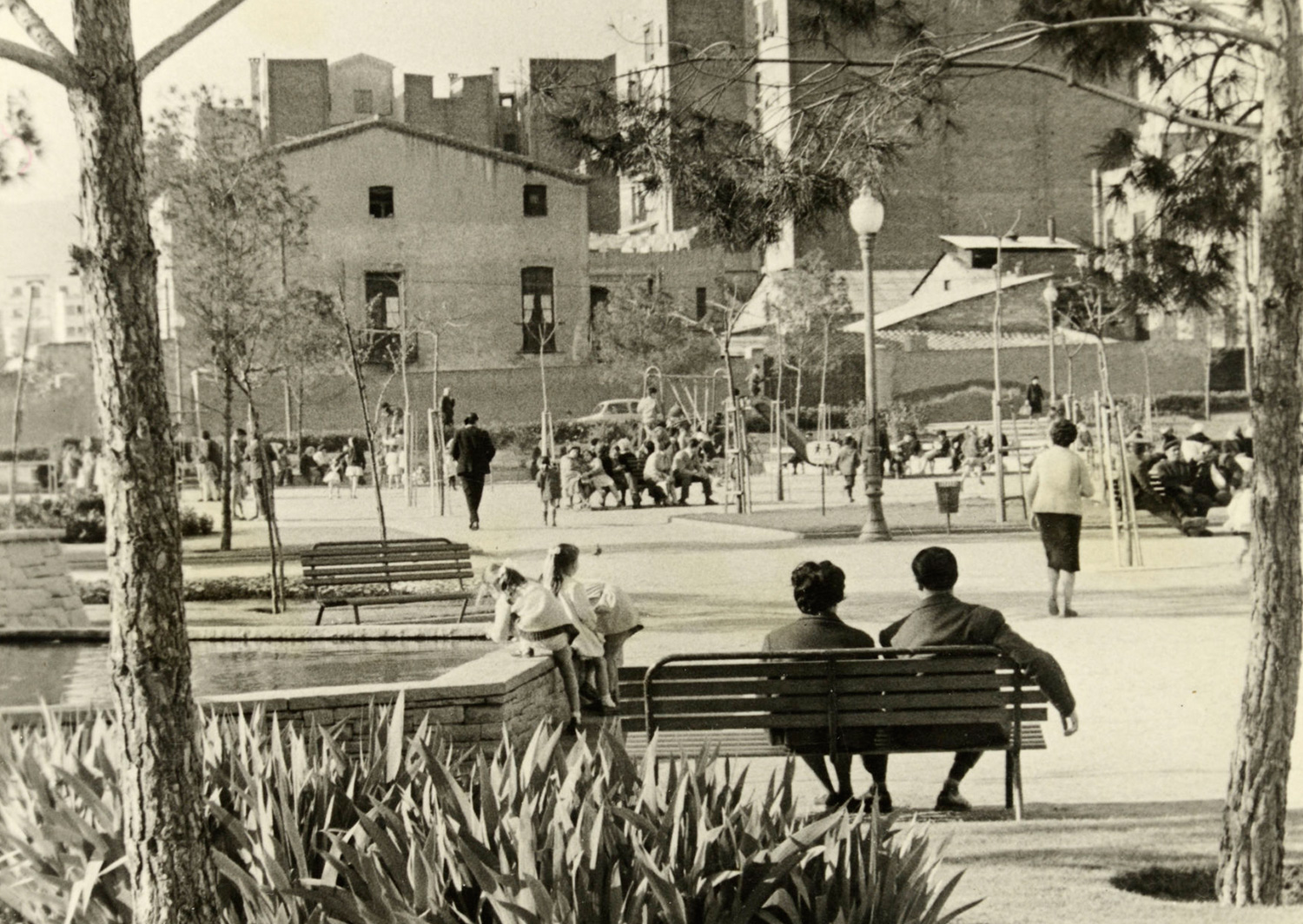 1963 AMDS Gent asseguda als bancs i nens jugant als jardins de can Mantega. Al fons, façana lateral de la masia de can Mantega. Autor Joan Janè